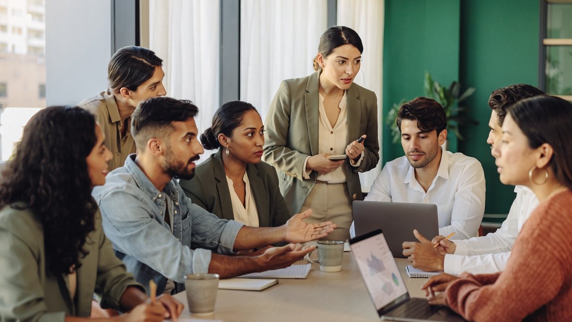 Equipo de trabajo reunido alrededor de una mesa con computadoras y notas adhesivas — evaluación 360 grados