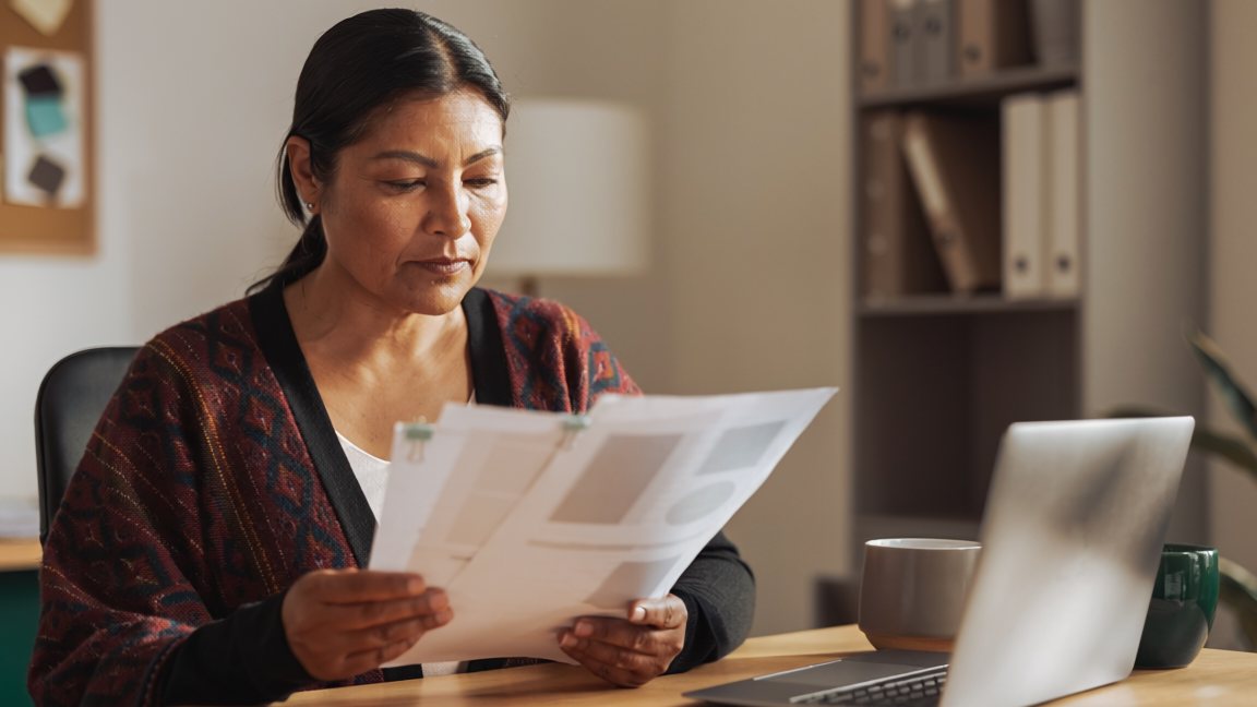 Mujer leyendo un informe impreso junto a su computadora — evaluación de competencias laborales